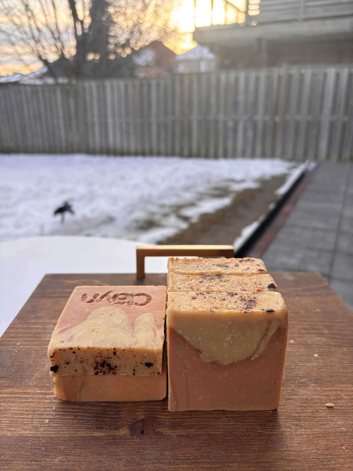 Two bars of soap on a wooden surface with a snowy backyard in the background