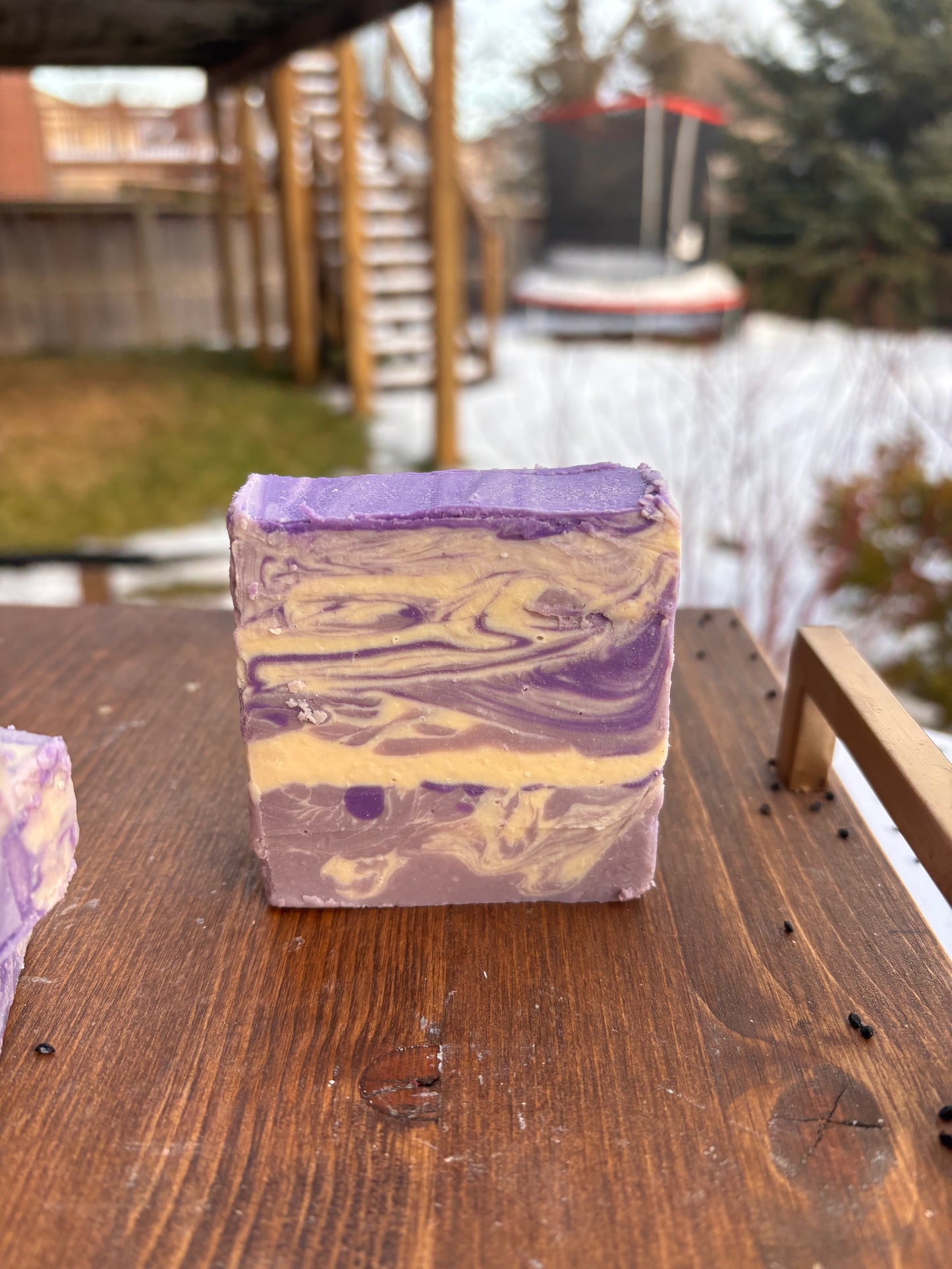 Bar of soap with purple and cream swirls on a wooden surface by a body of water.