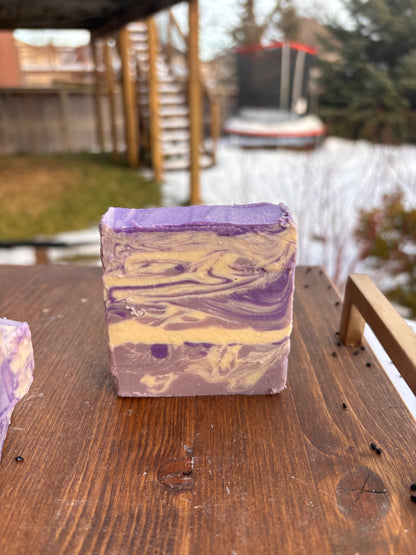 Bar of soap with purple and cream swirls on a wooden surface by a body of water.