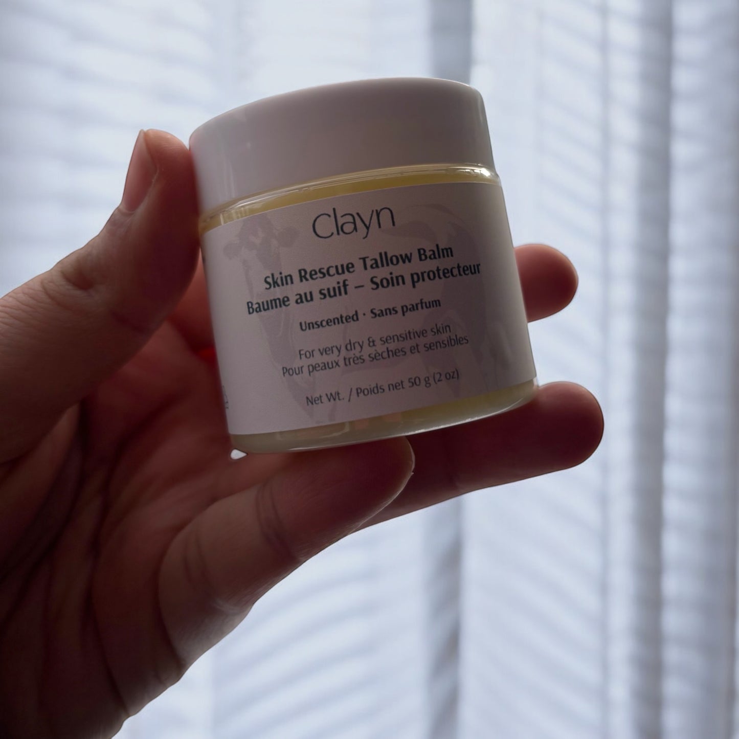 Hand holding a jar of Clayn Skin Rescue Tallow Balm against a blurred background