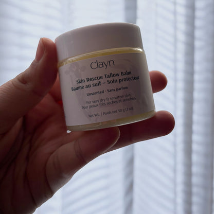 Hand holding a jar of Clayn Skin Rescue Tallow Balm against a blurred background