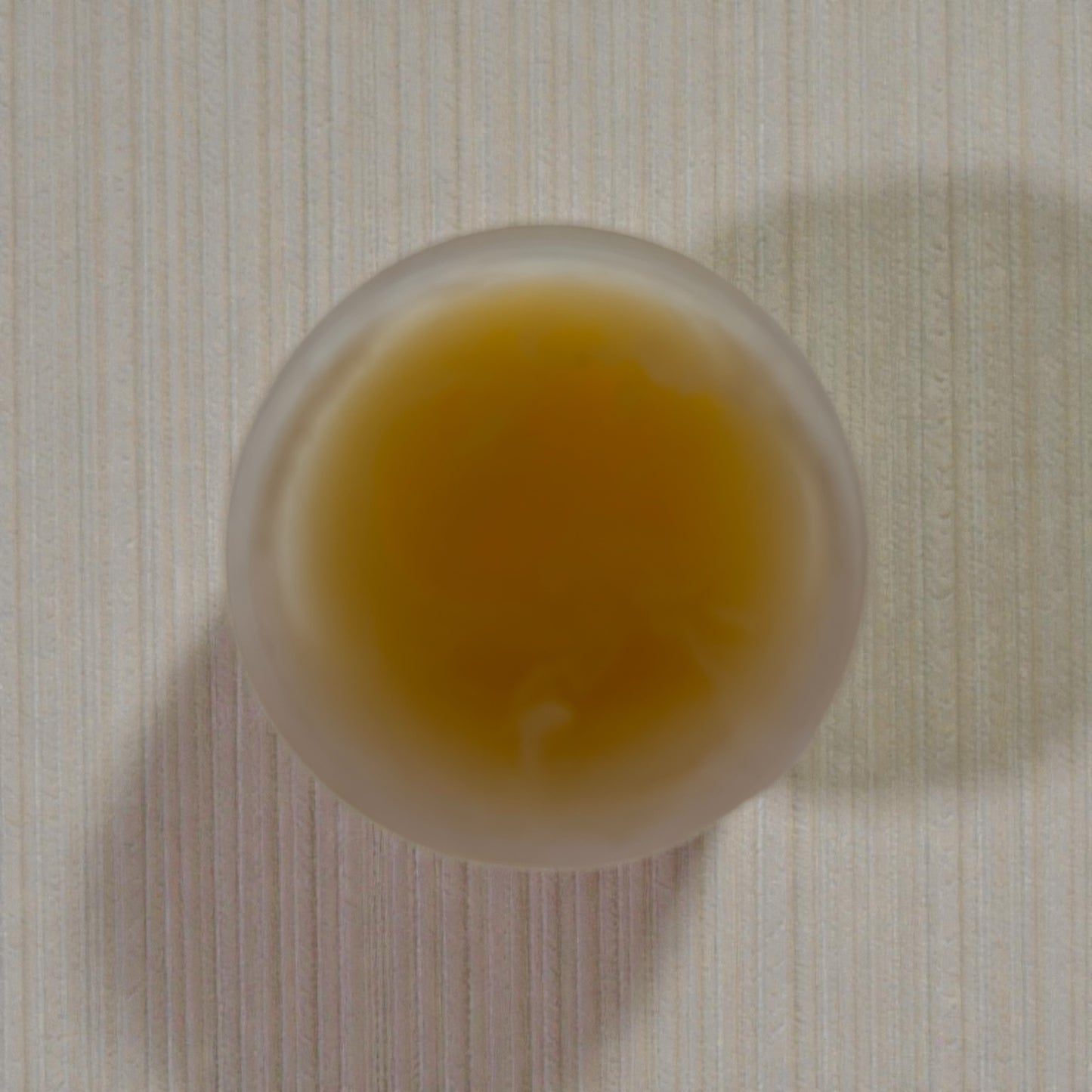 tallow balm container with a yellowish tallow balm on a textured surface
