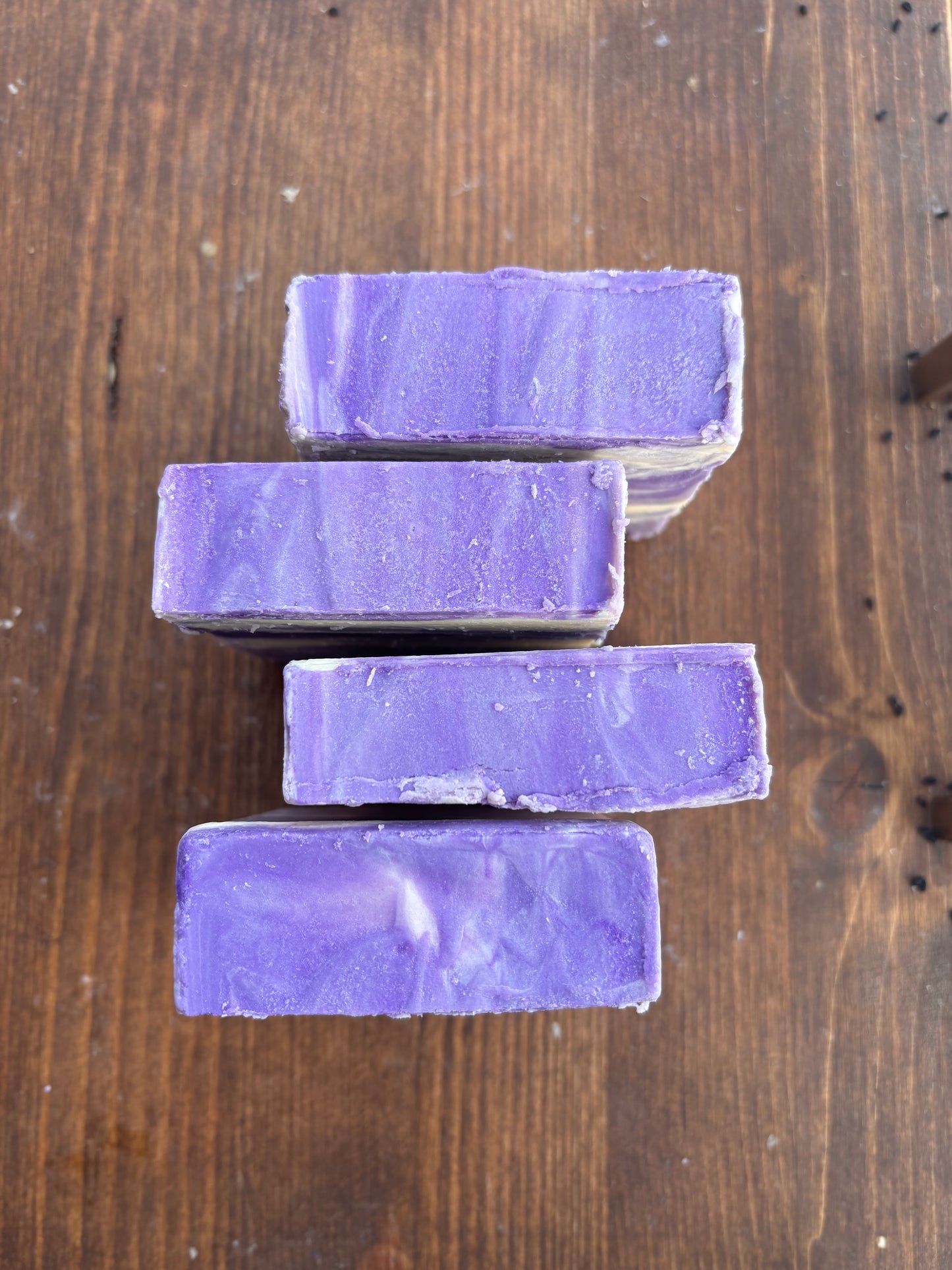 Four bars of purple soap stacked on a wooden surface